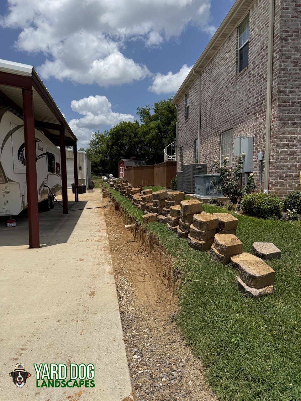 Old retaining wall blocks pulled and a trench excavated along the driveway during a wall rebuild in East Texas