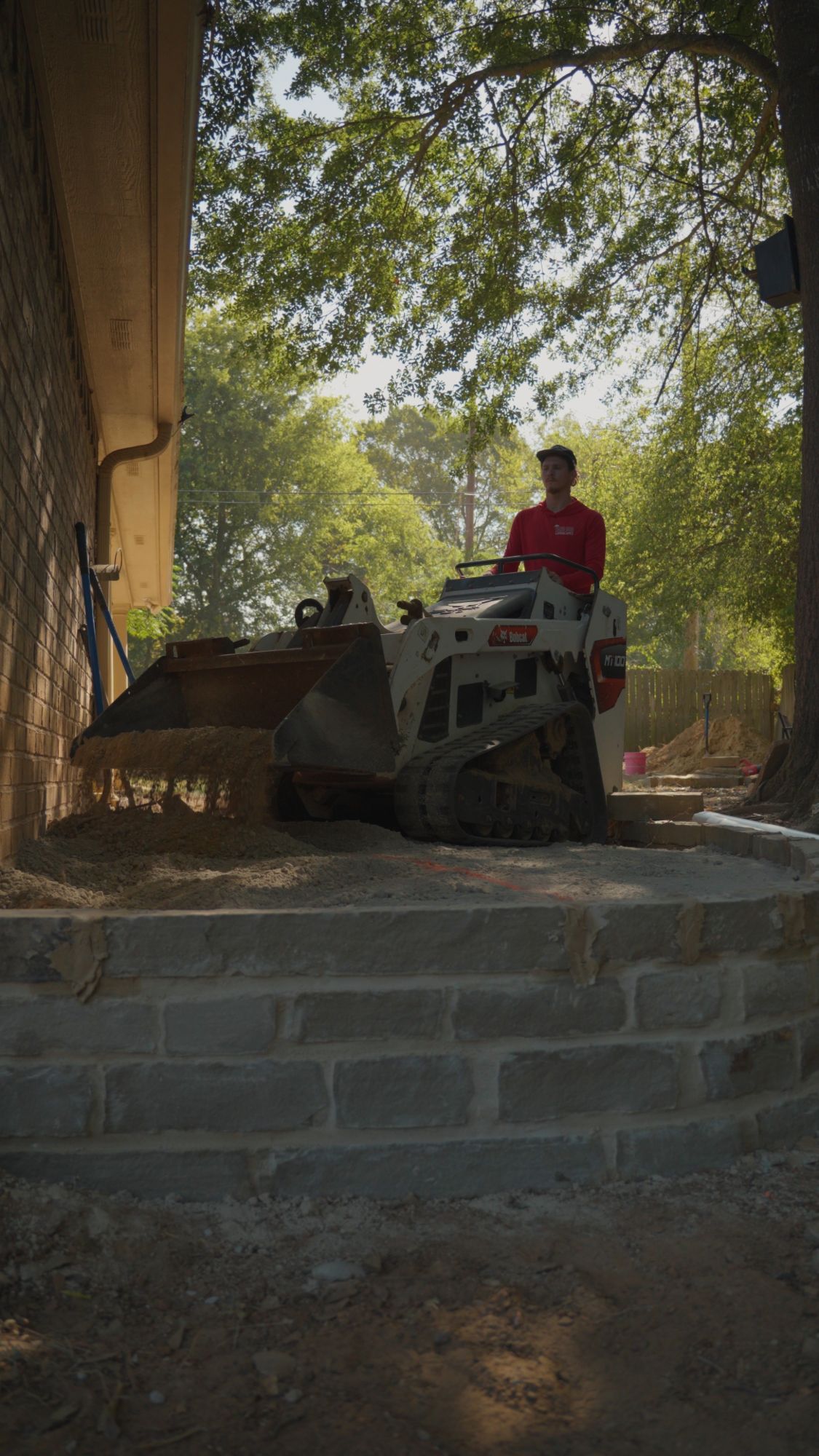 Track loader backfilling behind the mortared chopped stone elevated corner of a flagstone patio in White Oak, TX