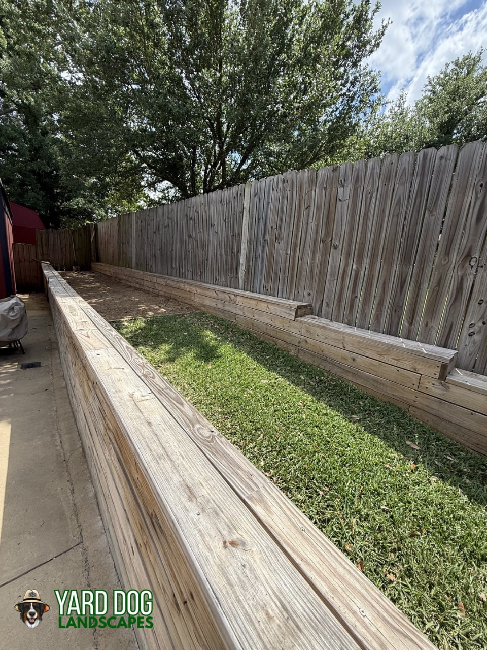 Old failing wood timber retaining wall along a backyard fence before Yard Dog Landscapes rebuilt it in East Texas