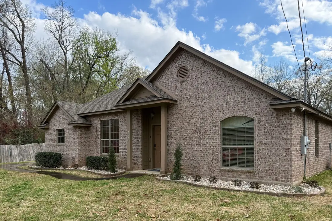 A brick ranch home in East Texas with white rock foundation beds and a bermuda lawn coming out of winter dormancy, patchy tan and green