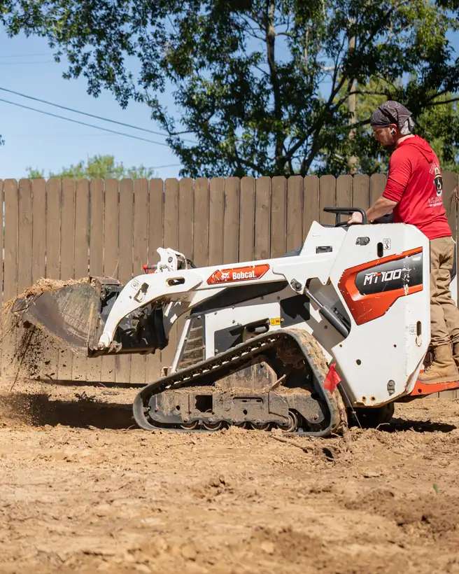 Mini track loader moving soil along the fence, Longview, TX